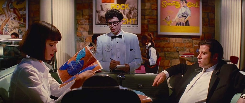 De Izquierda a Derecha: Mia Wallace (Uma Thurman), Vincent Vega (John Travolta) y en el medio, el mozo, Steve Buscemi, haciendo un cameo.