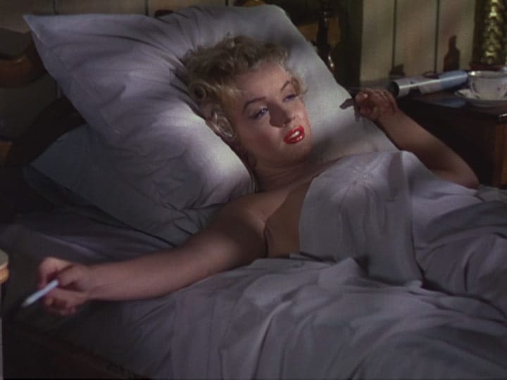 Marilyn Monroe acostada fumando un cigarro.