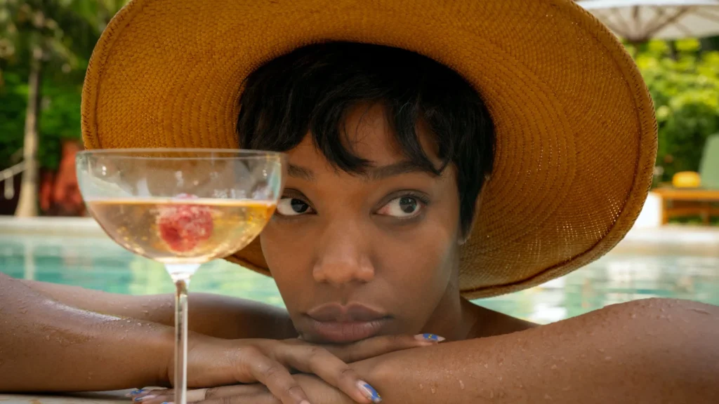 Naomi Ackie disfruta de un trago en la psicina, final explicado parpadea dos veces.