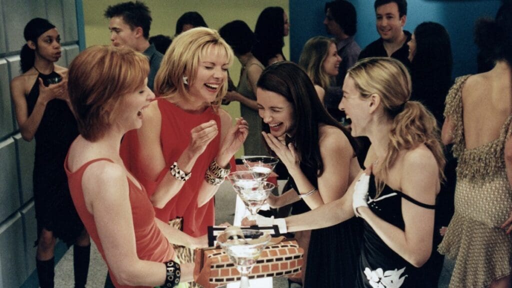 Escena de Sex and the City con Miranda, Samantha, Charlotte y Carrie riendo juntas en un bar