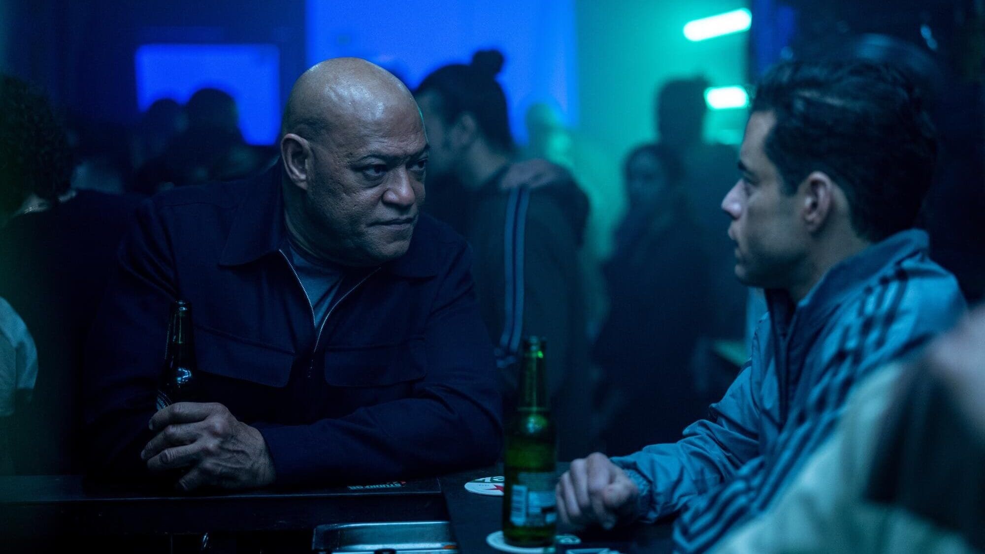 Laurence Fishburne y Rami Malek tomando cerveza en un bar en la película EL amateur