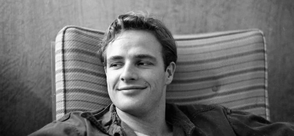 Retrato en blanco y negro de un joven Marlon Brando sonriendo en una silla