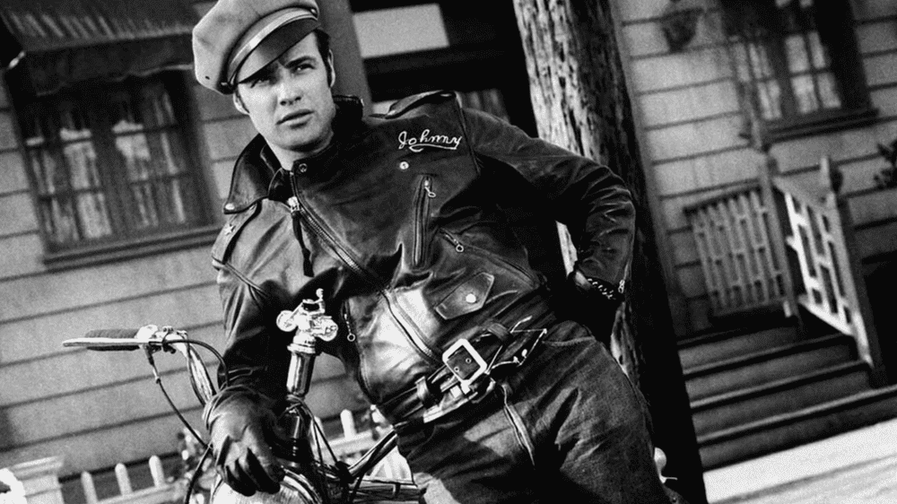 Marlon Brando como Johnny Strabler, apoyado en su motocicleta con chaqueta de cuero en The Wild One (1953)