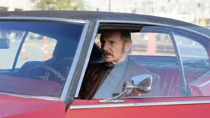 Liam Neeson en una escena de la película Absolution (Implacable), conduciendo un auto clásico.
