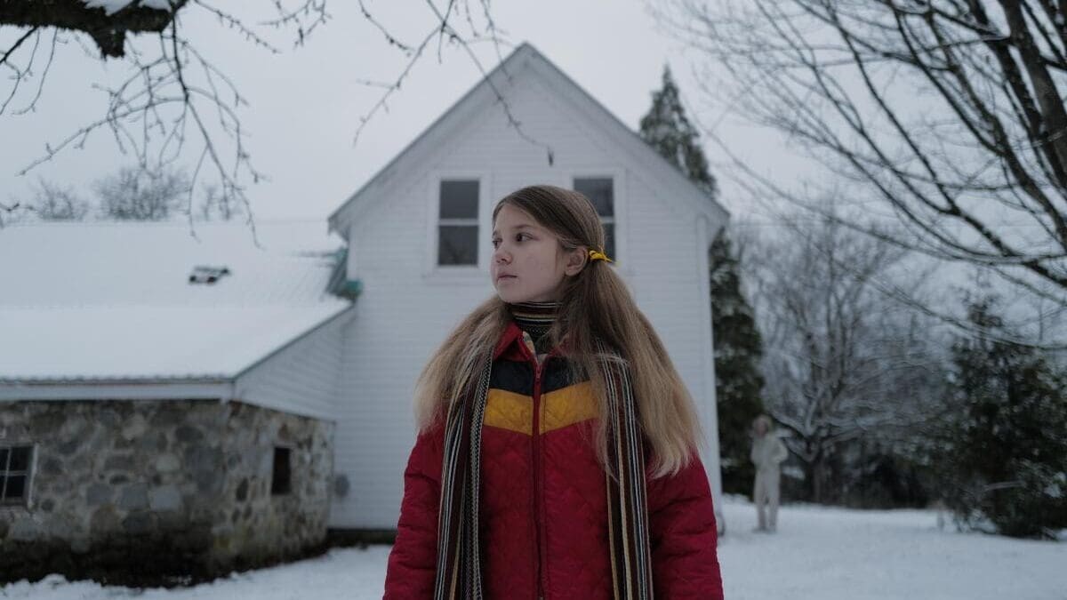 Escena de Longlegs (2024), la inquietante película de terror protagonizada por Maika Monroe, con una niña frente a una casa nevada que esconde un oscuro secreto.