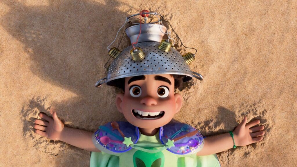 Elio acostado en la arena con un casco casero en la cabeza en una escena de la película animada de Pixar 'Elio' (2025)