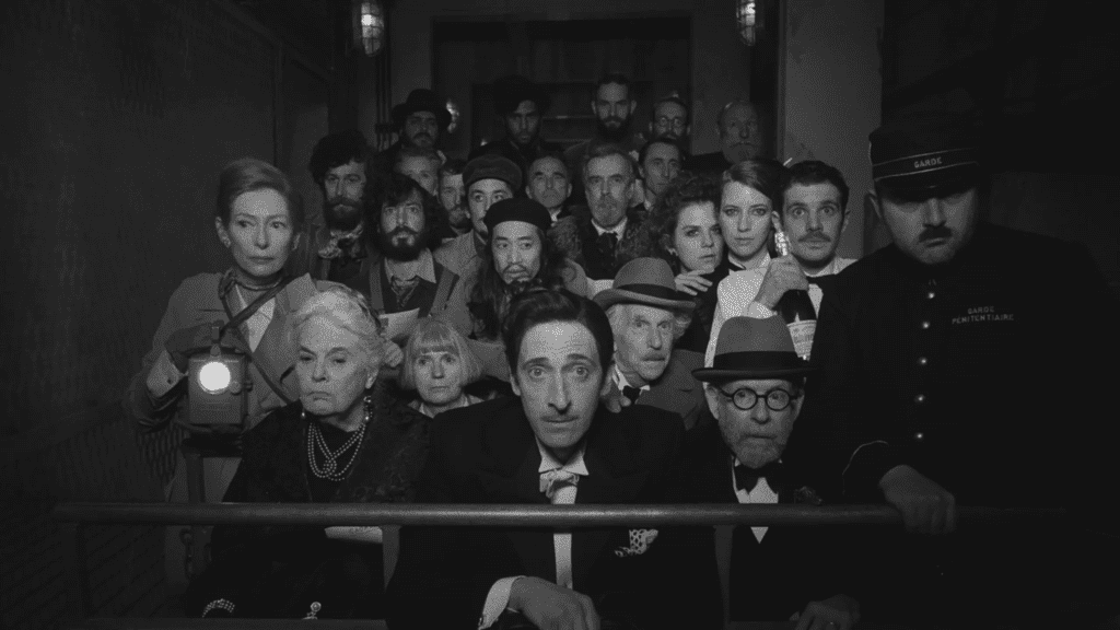 Escena en blanco y negro de "The French Dispatch" con Adrien Brody y elenco, dirigida por Wes Anderson.