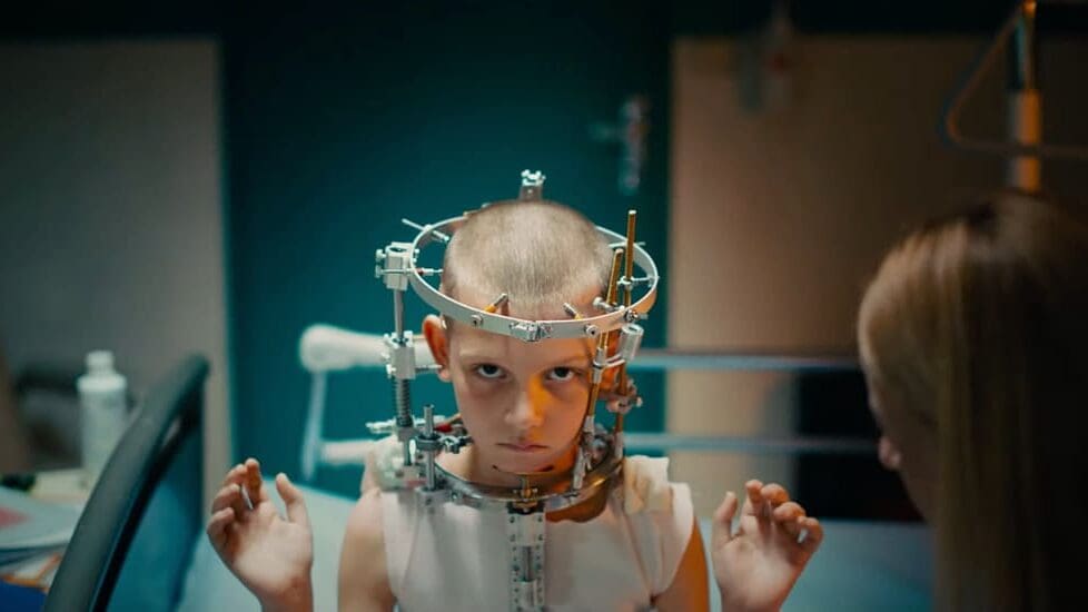 Niña con un halo craneal médico en una escena impactante de Titane (2021), la película de terror corporal dirigida por Julia Ducournau.