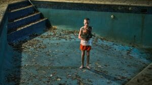 Niño con gato en piscina vacía cubierta de hojas en una escena inquietante de la película de terror Bring Her Back (2025)